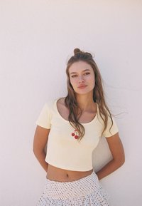 Gul crop top med rund halsringning och en röd körsbärsdesign. Kombinerad med en vit kjol prydd med svarta prickar.