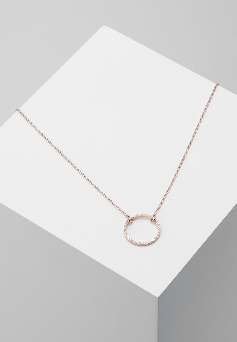 Collier délicat en or rose avec une fine chaîne et un pendentif circulaire texturé, présenté sur une surface géométrique blanche.