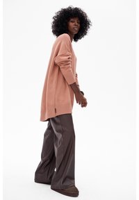 Jasnoróżowy oversize'owy sweter z prążkowanymi mankietami, zestawiony z ciemnobrązowymi spodniami o szerokich nogawkach i brązowymi butami wsuwanymi.