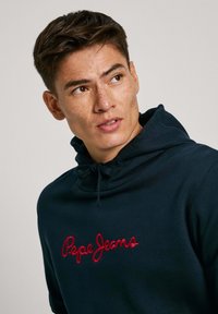 Felpa navy in tessuto morbido con cappuccio regolabile e logo "Pepe Jeans" ricamato in rosso sul davanti. Texture liscia.