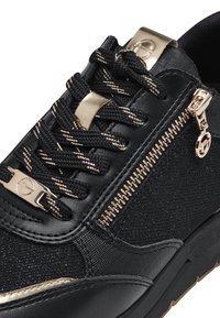 Sneaker nera con una parte superiore in tessuto testurizzato e pelle liscia. Accenti dorati includono i lacci e la cerniera, con suola in gomma robusta.