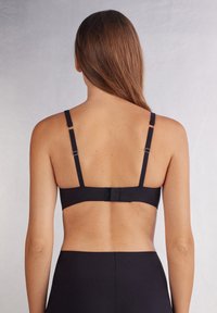 Svart bh med justerbara axelremmar, hak-och ögonslutning och slät tyg. Har minimala sömmar och en enkel design för komfort.