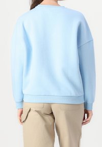 Sweat-shirt oversize bleu clair avec col rond et poignets côtelés, fabriqué dans un matériau doux. Vue de dos avec épaules tombantes et détails minimaux.