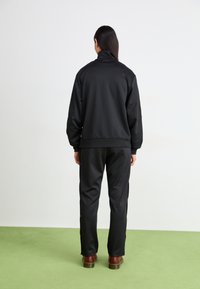 Casaco de fato de treino preto com gola alta e calças a condizer, feito de tecido suave. Apresenta punhos e cintura elásticos, usado com calçado castanho.