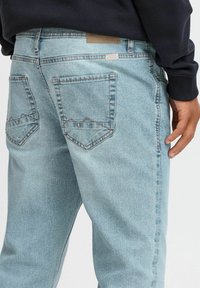 Vaqueros de mezclilla azul claro con un corte relajado, que cuentan con dos bolsillos traseros cosidos con patrones de zigzag y una pequeña etiqueta de la marca en la cintura.