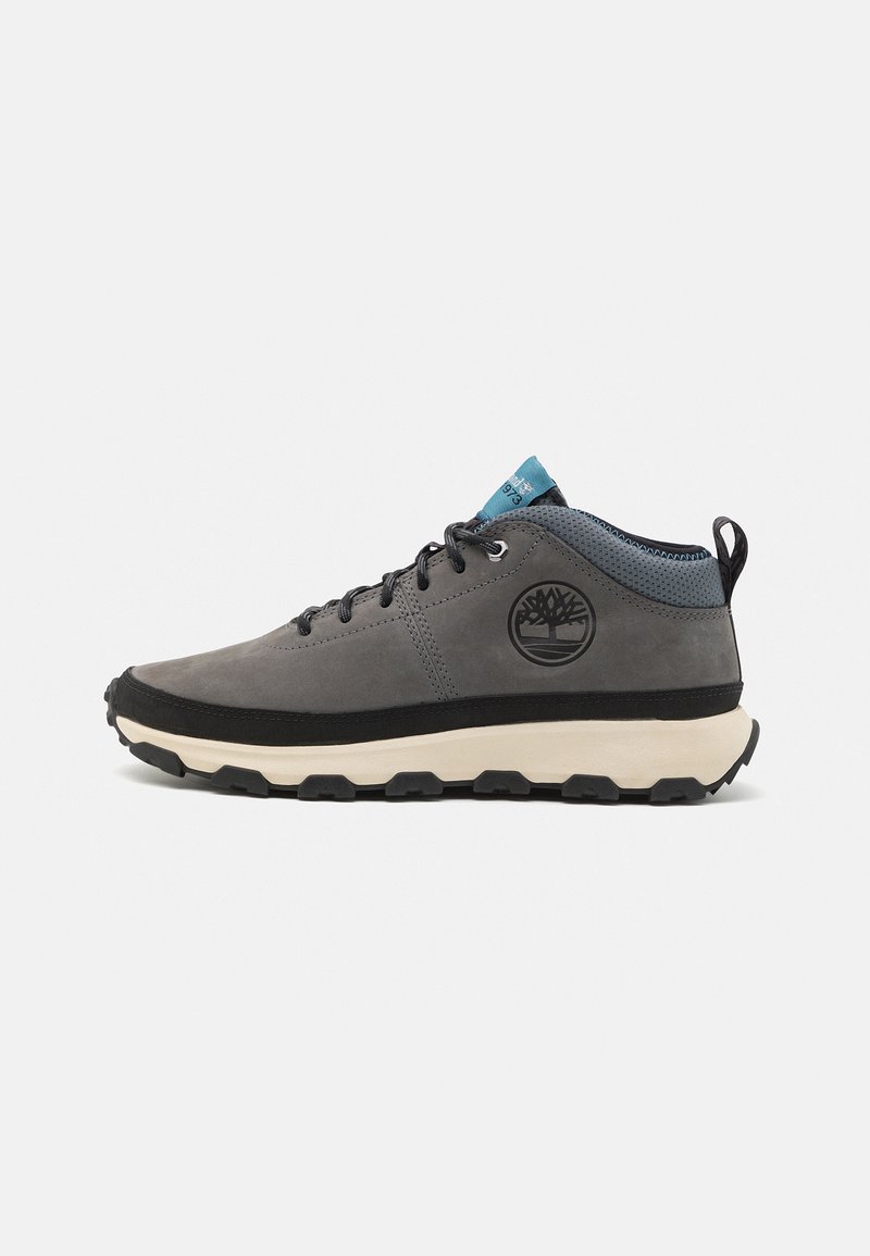 Las zapatillas impermeables grises cuentan con una parte superior lisa, suela negra con tacos circulares y un acento azul en la lengüeta con un detalle de logo.
