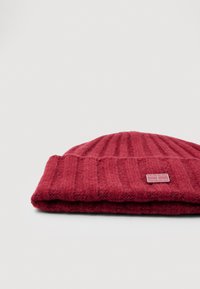 Kokkupandud punane soonikkoesbeanie, mille esiküljel on väike ristkülikuline Tommy Jeansi logopatch, halli ühevärvilise taustaga.
