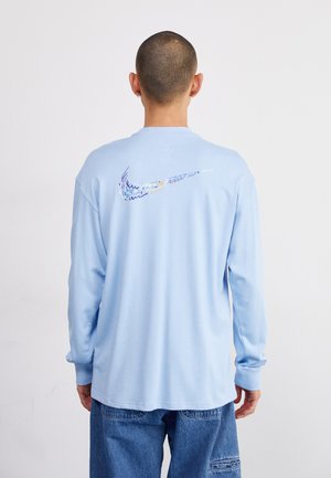 Cămașă cu mânecă lungă de culoare albastru deschis, cu guler rotund, având un logo Nike multicolor pe spate. Fabricată dintr-un material de bumbac moale.