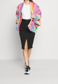 Cardigan de gran tamaño, colorido y con textura borrosa en tonos arcoíris mezclados, combinado con una camiseta blanca ajustada y una falda lápiz negra con una abertura frontal. Zapatillas deportivas negras.