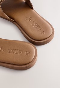 Sandales à glissière marron avec une tige en cuir lisse et une semelle épaisse texturée, présentant des détails de marquage embossés sur la semelle intérieure.