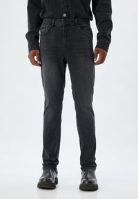 Jeans de denim negro con corte ajustado, que cuentan con un diseño clásico de cinco bolsillos, un sutil desgaste y se combinan con botas de cuero negro.