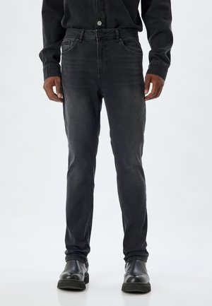 Jeans de denim negro con corte ajustado, que cuentan con un diseño clásico de cinco bolsillos, un sutil desgaste y se combinan con botas de cuero negro.