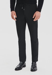 Czarne spódnie o dopasowanym kroju z elastycznym paskiem w talii, o wąskim kroju i gładkiej fakturze, w zestawieniu z wypolerowanymi czarnymi butami wizytowymi.