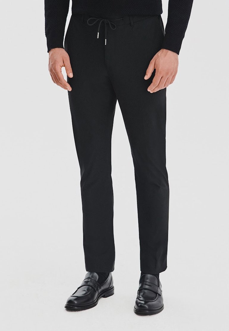 Czarne spódnie o dopasowanym kroju z elastycznym paskiem w talii, o wąskim kroju i gładkiej fakturze, w zestawieniu z wypolerowanymi czarnymi butami wizytowymi.