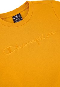Żółta bawełniana koszulka z haftowanym logo "Champion" i klasycznym dekoltem typu crew neck. Miękka tekstura z gładkim wykończeniem.