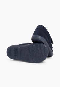 Des chaussures bleu foncé au toucher doux, avec une strap Velcro, une semelle en caoutchouc présentant un motif de semelle ondulé, et un texte en relief sur la semelle extérieure.