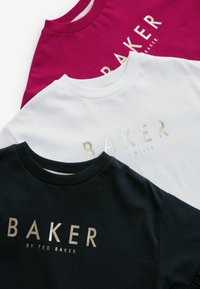 Trīs puloveri ar apaļām kakla izgriezumiem tumši zilā, baltā un fuksijas krāsā, uz kuriem priekšpusē ar zeltītiem burtiem ir vārds "BAKER".
