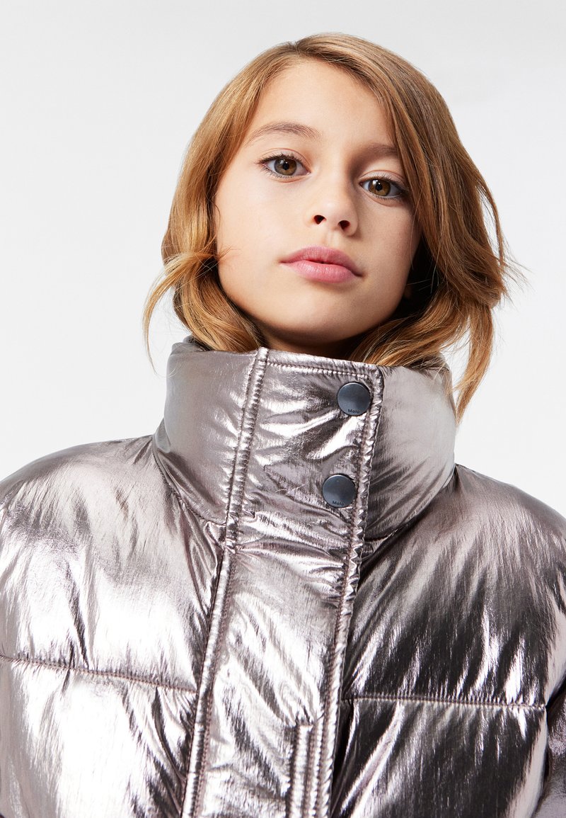 Metallisk puffjakke med høy krage, med glanset tekstur og to svarte knapper. Det quiltede designet fremhever varme og stil.