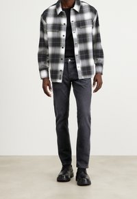 Randig skjorta i svart och vitt, knäppt med två bröstfickor, matchad med mörka jeans och svarta snörskor. Slät tygtextur.