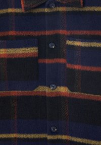 Maglia in pile di colore blu navy con un motivo a quadri rosso e giallo. Presenta due tasche sul petto e bottoni neri. Texture morbida con un aspetto accogliente.