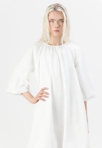 Hvit, hel lang kjole med rund utringning og puffede ermer. Laget av mykt stoff, med et løst og flytende design og samlet detaljer.