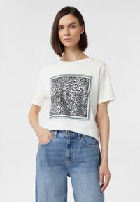 Baumwoll-T-Shirt mit kurzen Ärmeln in weißer Farbe, das mit einem auffälligen schwarzen und silbernen abstrakten Grafikdruck geschmückt ist, der von einem grünen Rahmen umgeben ist.