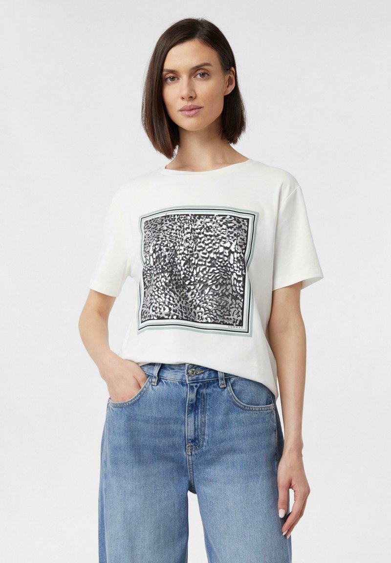 Baumwoll-T-Shirt mit kurzen Ärmeln in weißer Farbe, das mit einem auffälligen schwarzen und silbernen abstrakten Grafikdruck geschmückt ist, der von einem grünen Rahmen umgeben ist.