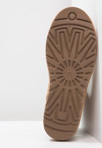 Podeszwa brązowego buta UGG z teksturowaną gumową powierzchnią z geometrycznym wzorem i okrągłym akcentem w okolicy pięty.