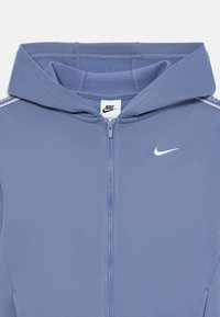 Svetlomodrá Nike mikina na zips s vysokým golierom a kapucňou, obsahujúca malé biele logo na hrudi a kontrastné bočné detaily.