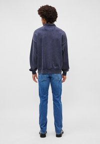 Sweatshirt bleumarin cu guler înalt și croială lejeră, asortat cu blugi drepți de un albastru deschis. Textura denimului este vizibilă.