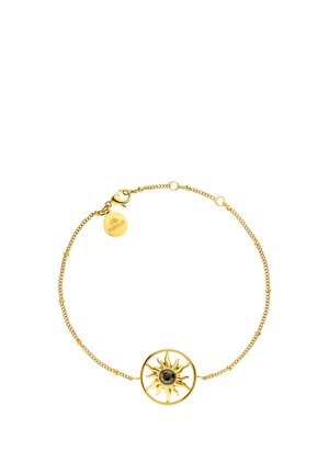 Delicate gold chain bracelet with sun-shaped charm featuring a central dark gemstone and a small engraved round tag near the clasp.