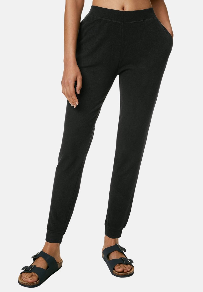 Pantalones de chándal negros hechos de tela suave, con piernas ajustadas, cinturilla elástica y bolsillos laterales, combinados con sandalias oscuras.