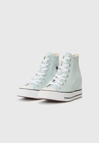 Vysoké tenisky vo svetlom mätovom plátne s bielymi šnúrkami, čiernym pruhom na podrážke a textúrovaným gumovým špičkou. Logo Converse na boku.