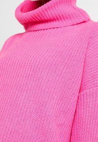 Jasnoróżowy sweter typu golf z dzianiny, o prążkowanej teksturze i grubym, przytulnym materiale, pokazany od talii do szyi.