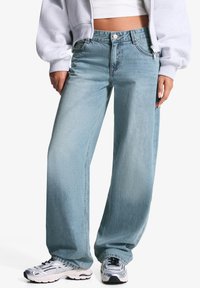 Blugi lejera de culoare albastru deschis, din denim, cu talie înaltă, cusături vizibile și o ușoară decolorare. Purtați cu adidași argintii.