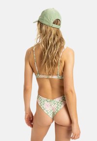 Swimwear set featuring a pink and green leaf pattern with thin straps and high-cut bottoms. Paired with a light green cap.