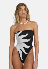 Sort-hvitt stroppeløst badedrakt med solstrålegrafikk, høyt utskjærte ben og teksturert stoff. Hvit perlekjede brukt.