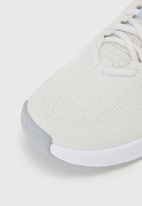 Light grey athletic shoe featuring a textured mesh upper, padded tongue, and a white rubber sole with a grey accent on the toe cap.