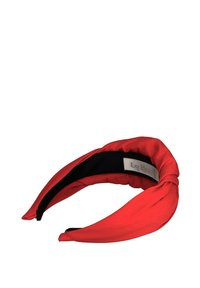 Czerwona opaska na głowę z skręconym wzorem, z czarnym wykończeniem od środka i metalową zawieszką z logo z boku. Gładka tekstura na całej powierzchni.