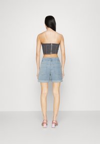 Top sin tirantes de mezclilla negra con cremallera en la espalda, combinado con pantalones cortos de mezclilla azul claro con dobladillo enrollado y bolsillos delanteros y traseros.