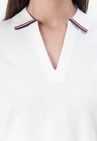 Polo blanc à col en V, avec un col contrastant aux rayures rouges et bleu marine, fabriqué en tissu texturé.