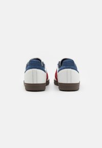White sneakers with red and blue accents. Textured heel and side panels. Rubber sole, cushioned collar, and stitched detailing.