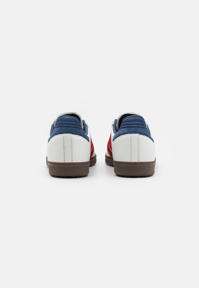 Zapatillas blancas con acentos en rojo y azul. Tacón con textura y paneles laterales. Suela de goma, cuello acolchado y detalles de costura.