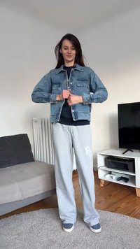 Hele sinine teksajakk esitaskutega, must T-särk, hallid dressipüksid ja mustriga libisemiskindlad kingad. Siseinterjöör, neutraalne taust.