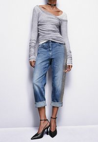 Top gris de manga larga, ajustado en los hombros, combinado con unos vaqueros de puños enrollados en azul claro y tacones negros puntiagudos con tiras en el tobillo.