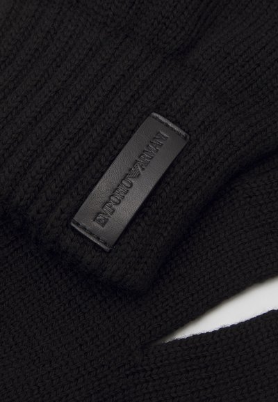 Svart stickade handskar med ett texturerat mönster och en rektangulär svart läderetikett med präglat varumärke.