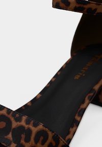 Sandale à imprimé léopard marron et noir avec talon bloc et fine bride à la cheville, semelle intérieure noire avec texte de marque orange.