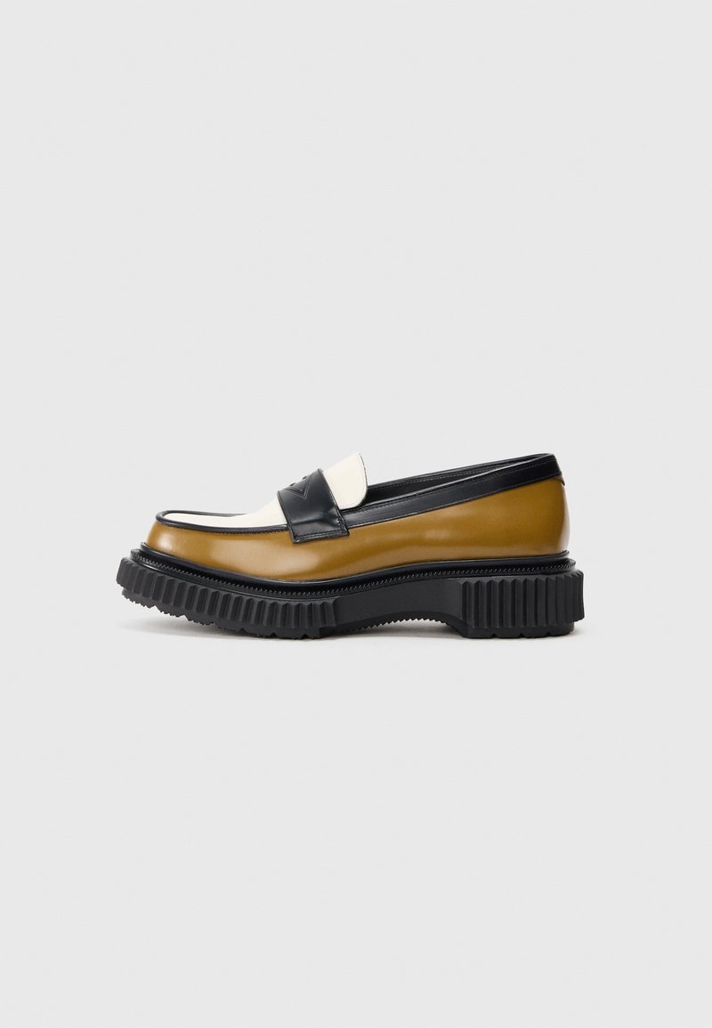 Mocassin à semelle épaisse avec panneaux en cuir marron, blanc et noir, et semelle extérieure en caoutchouc noir nervurée, présenté de profil sur fond gris.