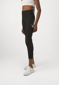 Svarta sportleggings med hög midja, med en vit logotyp på sidan, gjorda av stretchigt material för flexibilitet. Parat med vita sneakers.