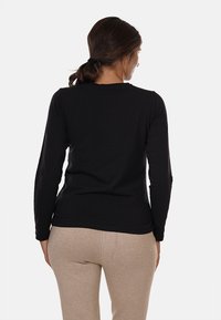 Maglietta nera a maniche lunghe realizzata in tessuto morbido, con scollo rotondo e design aderente. Indossata con leggings beige.